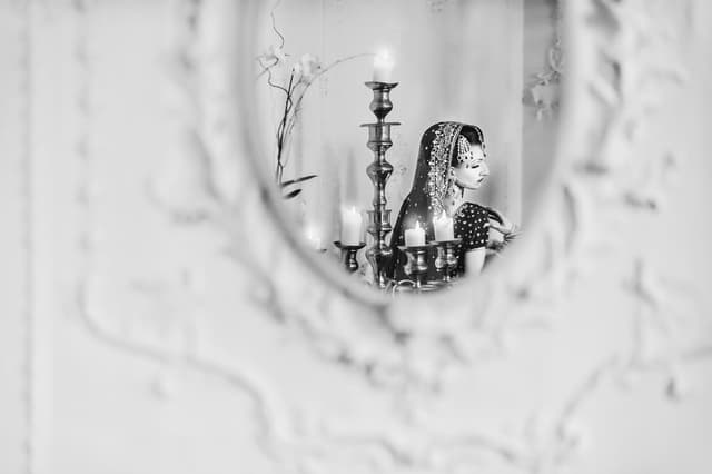 Bride in traditional attire seen in a mirror with candles, color correction for a moody look, background cleanup, and skin retouching kept natural