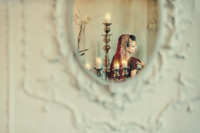 Bride in traditional attire seen in a mirror with candles, color correction for a moody look, background cleanup, and skin retouching kept natural