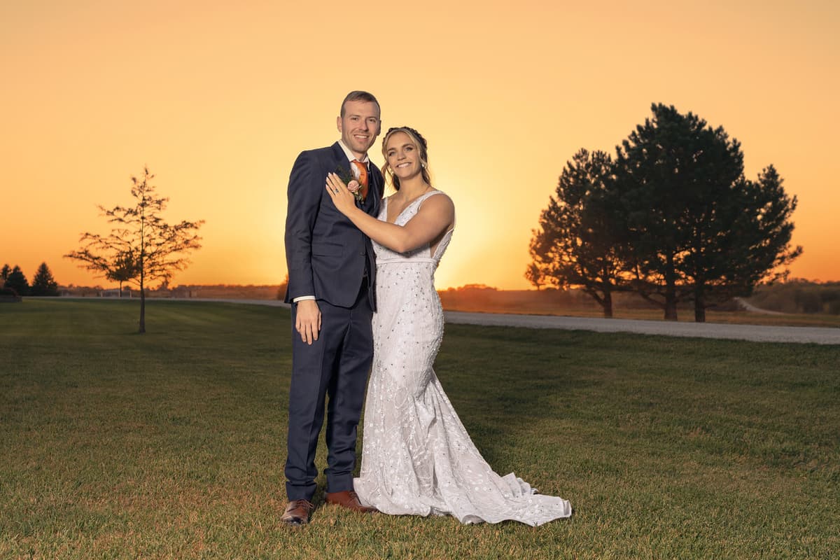 Wedding couple hugging on lawn at golden hour, consistent tones across the image, background cleanup, and subtle skin retouching with natural texture