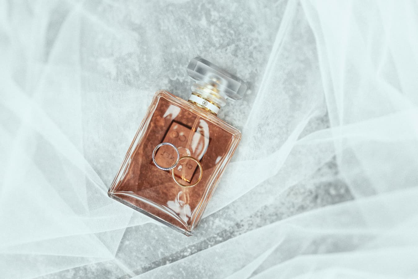 Wedding rings on a perfume bottle with white bridal veil