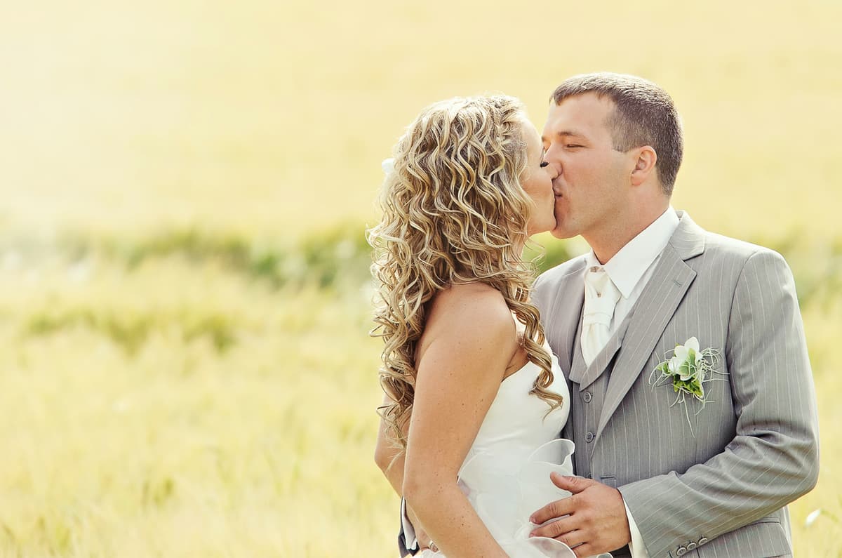 Bride and groom kissing in a sunny field with golden bokeh background