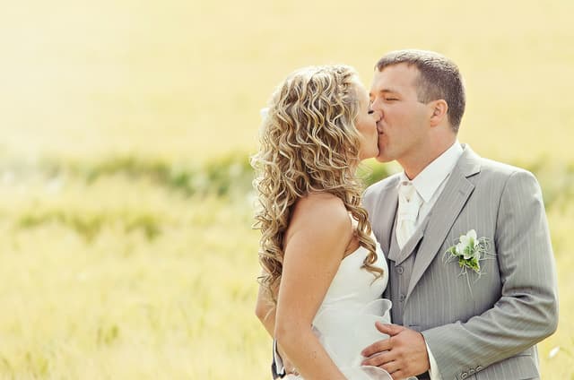 Bride and groom kissing in a sunny field with golden bokeh background