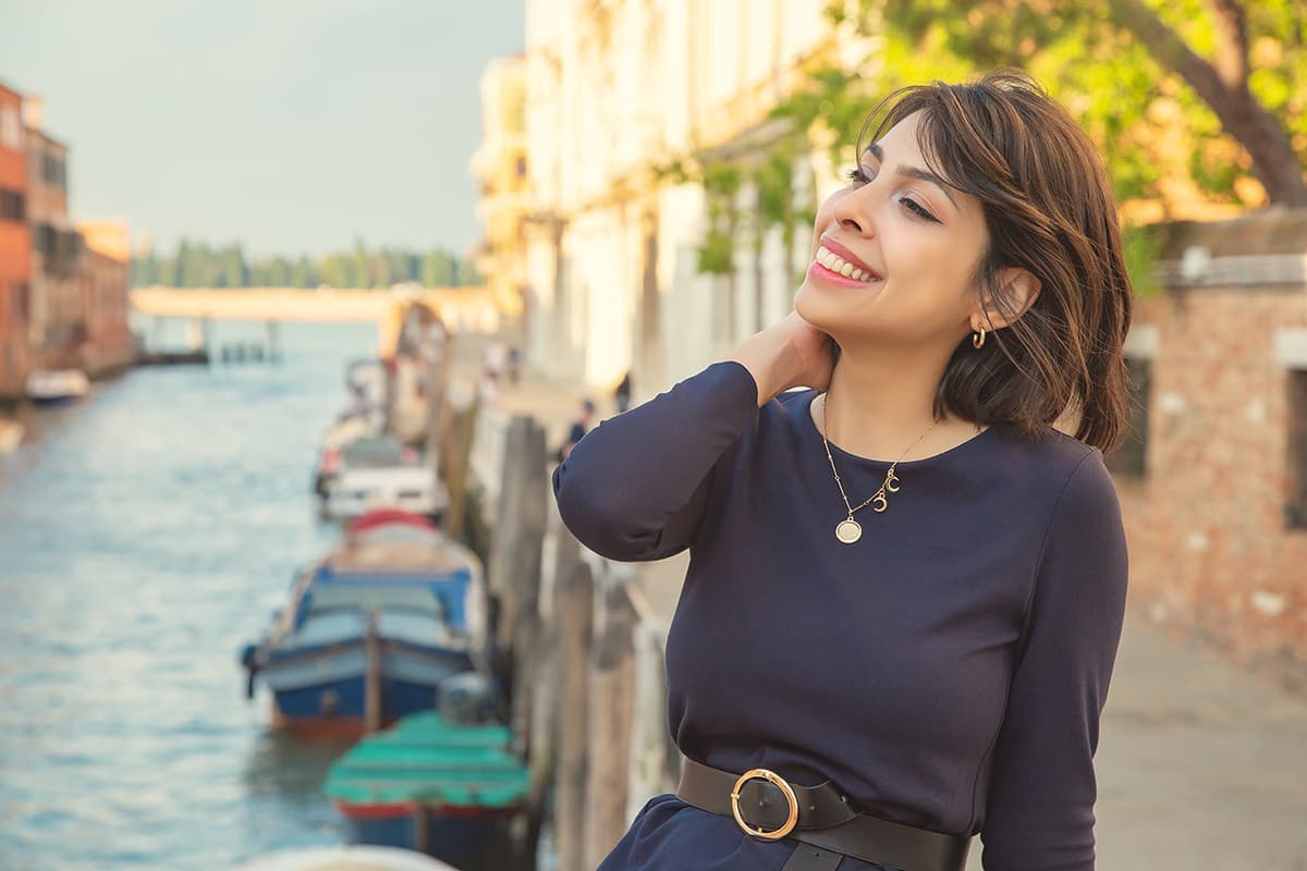 Smiling woman portrait by a Venice canal with boats; skin and beauty retouching, hair and eyes enhancement, and color correction