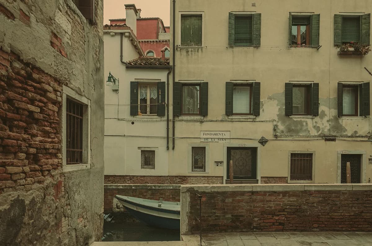 Quiet Venice canal with a small boat and aged facades; background cleanup, color correction, and artistic grading for a soft editorial travel look