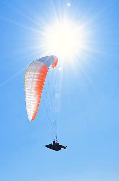 Paraglider flying below a bright sun in clear blue sky; color correction, background cleanup, matching tones across the set