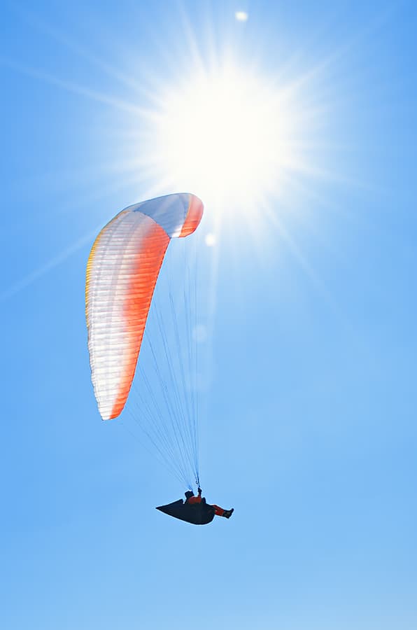 Paraglider flying below a bright sun in clear blue sky; color correction, background cleanup, matching tones across the set